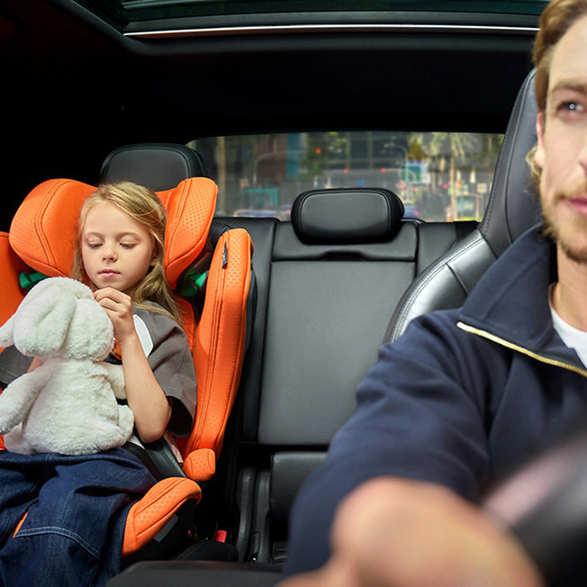 Mand kører bil mens pige sover i Recaro Axion 1 autostol med bamse, orange model