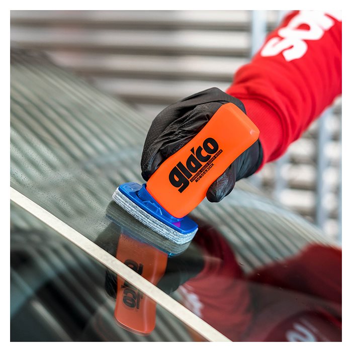 Hand mit Glaco DX Glasversiegelung auf Autoscheibe in der Nähe von weißem Klebeband