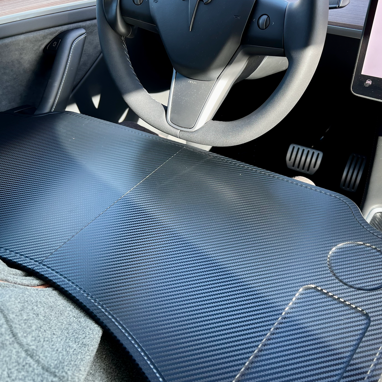 Klappbarer Tisch in dunklem Carbon-Look, gesehen im Inneren eines Tesla-Autos