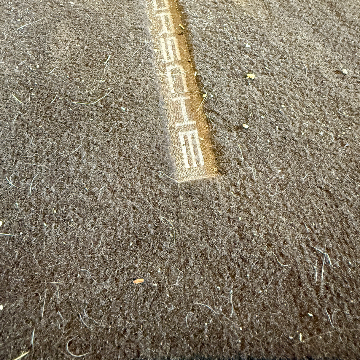 Vorher-Bild einer stark verschmutzten Autofußmatte mit Porsche-Logo vor dem TurboClean Staubsauger
