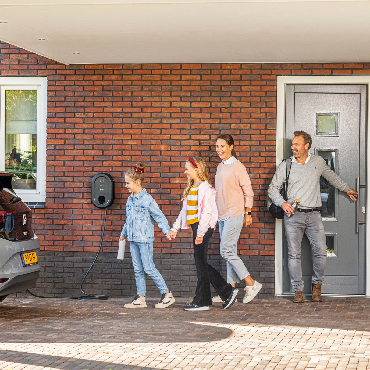 Familie kommt nach Hause zu einer Ratio-Ladestation und einem angeschlossenen Elektroauto