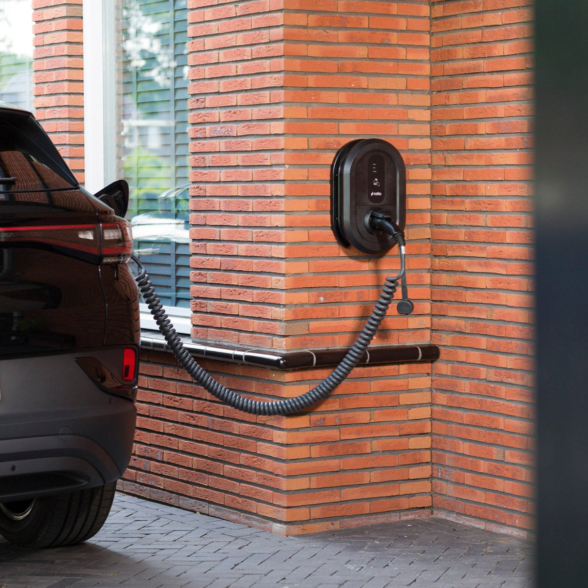 Ratio-Ladegerät an einer Ziegelwand montiert, das ein schwarzes Elektroauto auflädt