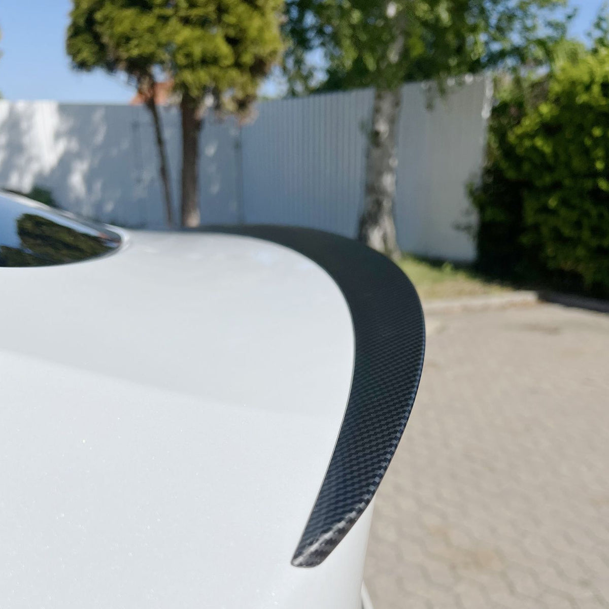 Spoiler i carbon-look monteret på bagklappen af en hvid Tesla Model Y, udendørs