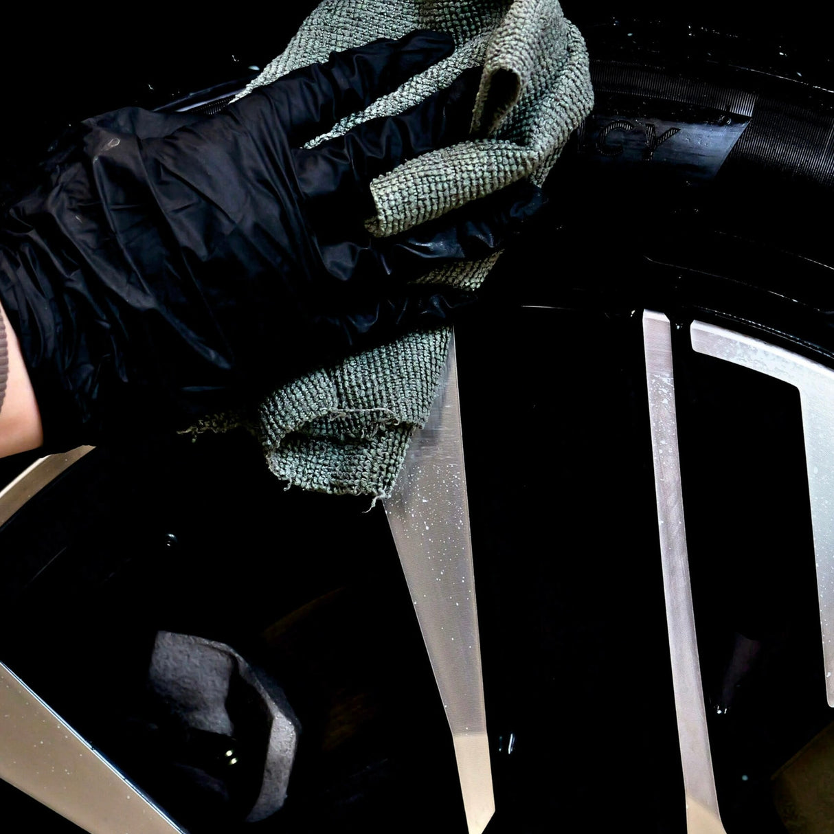 Hand mit Handschuh trägt Autoland Reifenpflege mit einem Tuch auf einen Autoreifen auf.