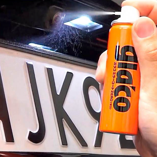 Hand, die Glaco Mirror Coat Zero auf eine Autokamera über dem Nummernschild sprüht.