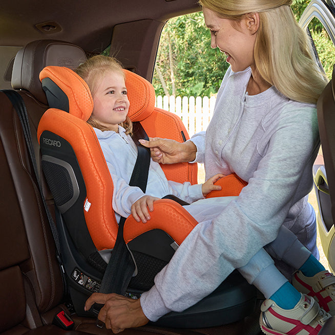 Mor spænder barn fast i Recaro Xenon 1 Kid autostol i bilen, begge smiler