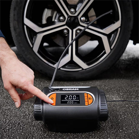 Person trykker på knap på Osram TYREinflate 2120 kompressor foran bildæk