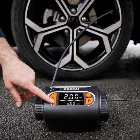 Person trykker på knap på Osram TYREinflate 2130 kompressor foran bildæk