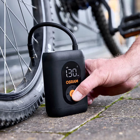 Hånd trykker på knap på Osram TYREinflate 1600 ved cykelhjul, display viser 130
