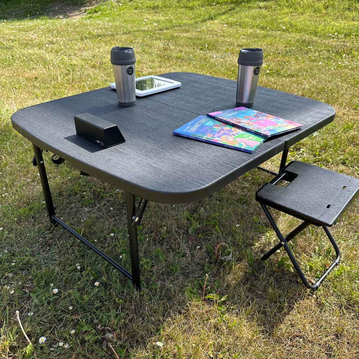 schwarzer Campingtisch mit Kaffeetasse, Kinderbüchern und einem Tablet