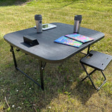 schwarzer Campingtisch mit Kaffeetasse, Kinderbüchern und einem Tablet