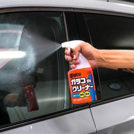Person sprüht Glaco-Reiniger auf die Autoscheibe, um Wasser zu entfernen.