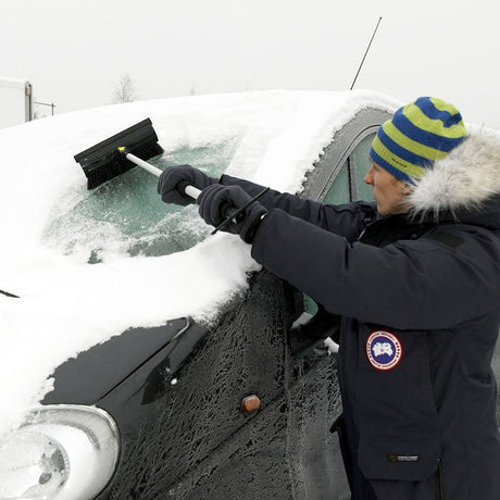 Mann, der Schnee von der Windschutzscheibe eines Autos kratzt
