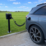 Ein schwarzes Spiralladekabel, das an eine Ladestation und ein Elektroauto angeschlossen ist