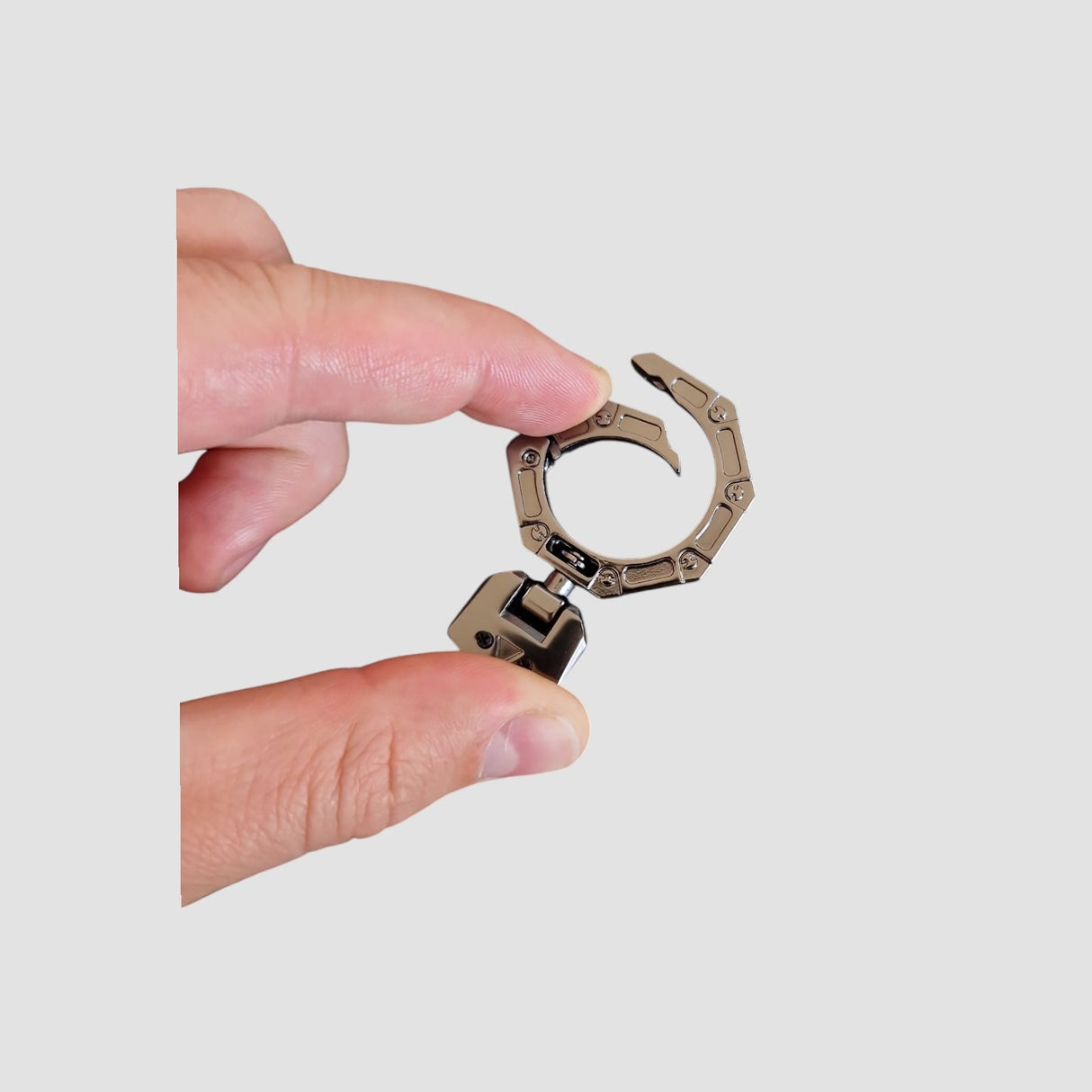Person hält eine Schlüsselhülle/-ring für Toyota bZ4X zwischen zwei Fingern vor neutralem Hintergrund.