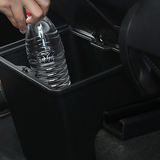 Schwarze Abfallaufbewahrungsbox mit Klappdeckel im Inneren eines Autos, mit einer Wasserflasche darin.