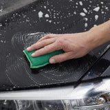 Hand wäscht Auto mit grünem Schwamm und Seifenblasen.