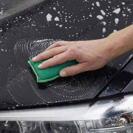 Hand wäscht Auto mit grünem Schwamm und Seifenblasen.