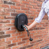 Hand setzt Typ-2-Ladekabel in Ratio intelligenten Ladebox an einer Ziegelwand ein