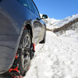 Schneeketten montiert auf einem grauen Autoreifen in schneebedeckten Bergen
