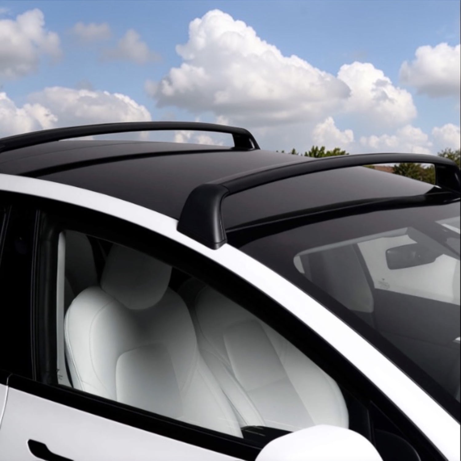 Tesla Model Y mit schwarzen Dachträgern unter einem blauen Himmel mit Wolken